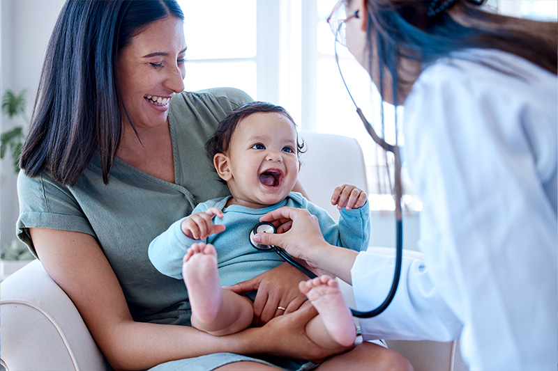 Woman holding baby who is being tended to by a physician.