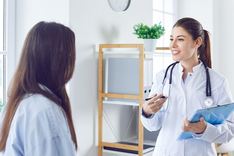 Physician speaking to female patient about hypertension, physician is holding a blue clipboard.